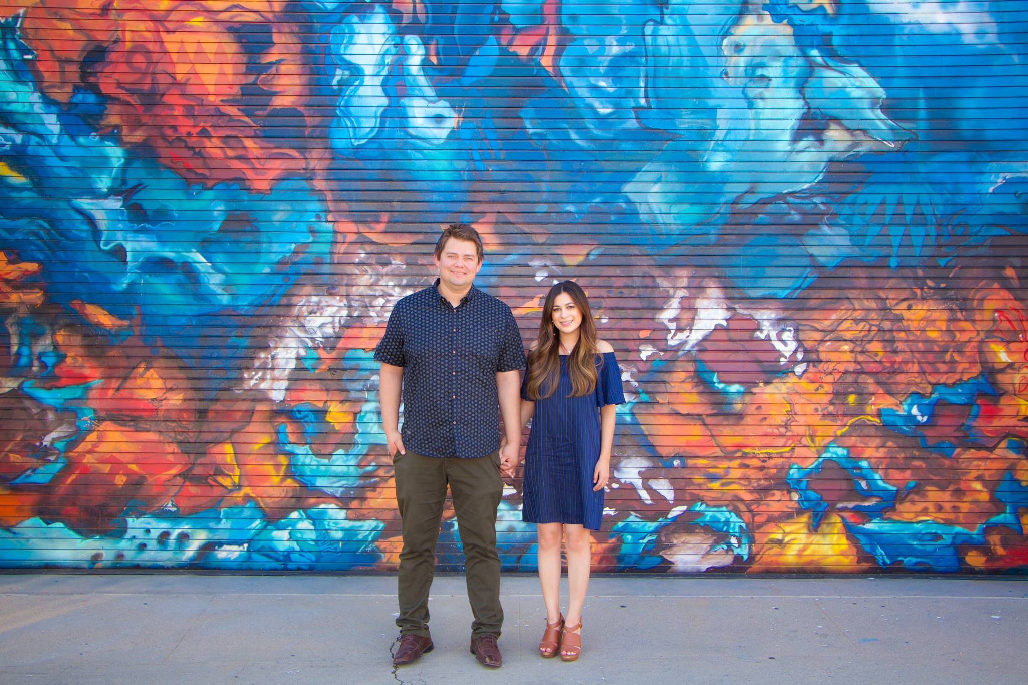 choosing engagement outfits for couple standing by artistic wall